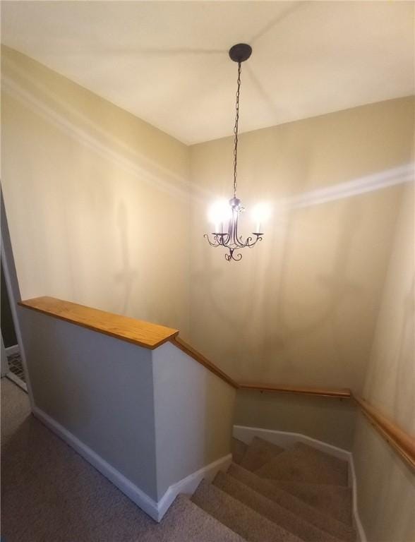 stairway with an inviting chandelier, baseboards, and carpet floors