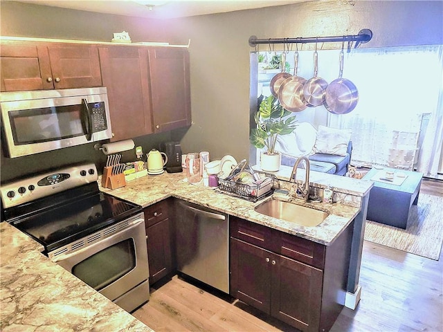 kitchen with light wood-style flooring, a sink, stainless steel appliances, a peninsula, and light stone countertops