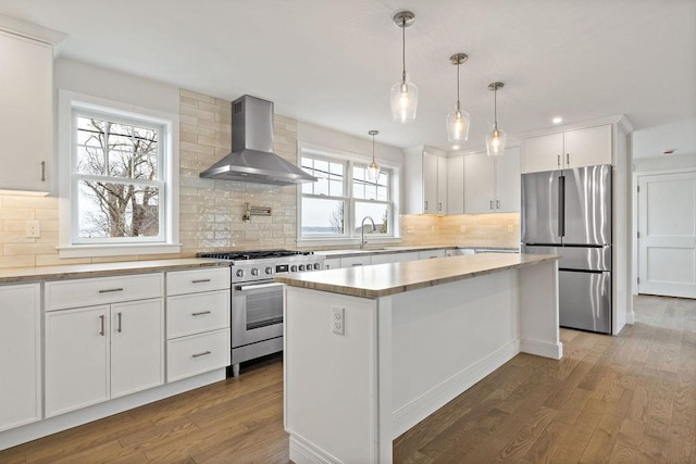 kitchen with wall chimney range hood, light countertops, appliances with stainless steel finishes, wood finished floors, and white cabinets