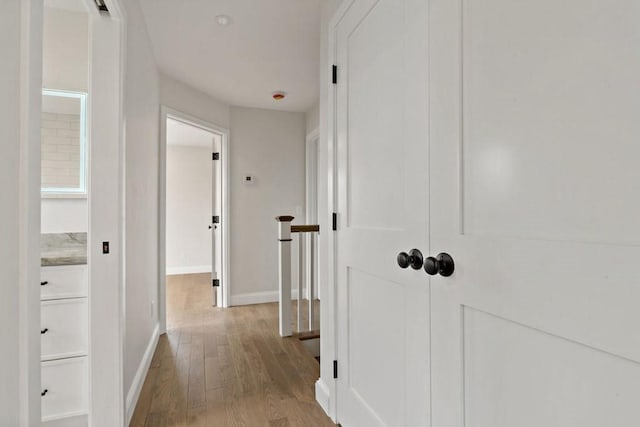 corridor with an upstairs landing, wood finished floors, and baseboards