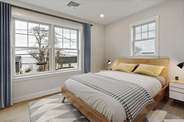 bedroom featuring visible vents, multiple windows, baseboards, and wood finished floors