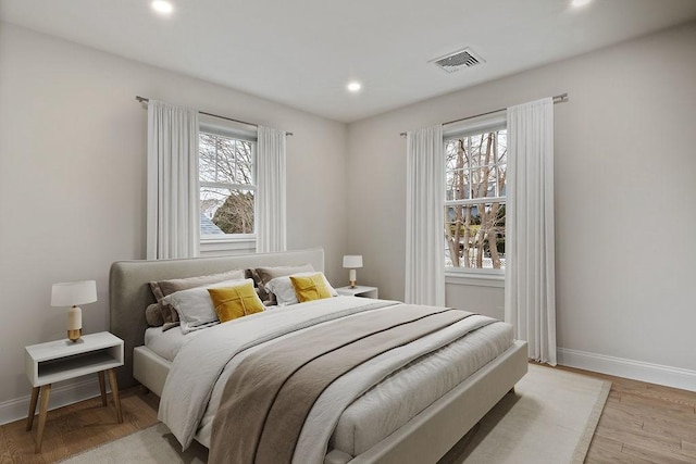 bedroom with multiple windows, light wood-style floors, and baseboards