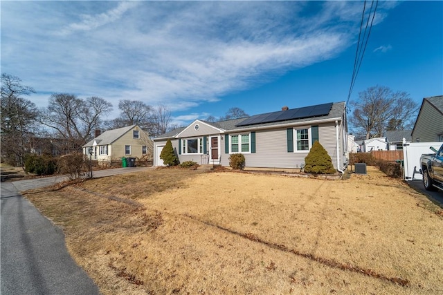 ranch-style home with fence, central air condition unit, roof mounted solar panels, a garage, and driveway