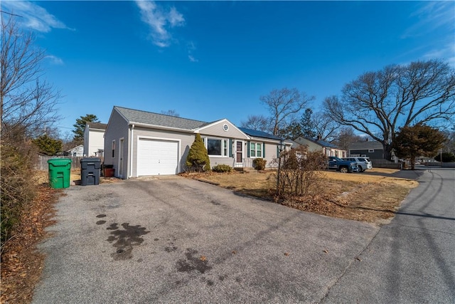 ranch-style home with a garage, solar panels, and aphalt driveway