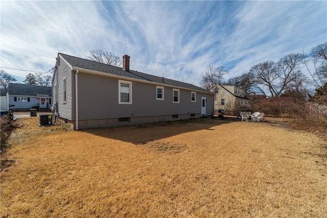 rear view of property featuring central air condition unit, a chimney, and a yard