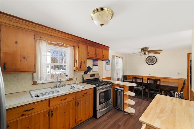 kitchen with brown cabinetry, light countertops, stainless steel range with gas cooktop, and a sink