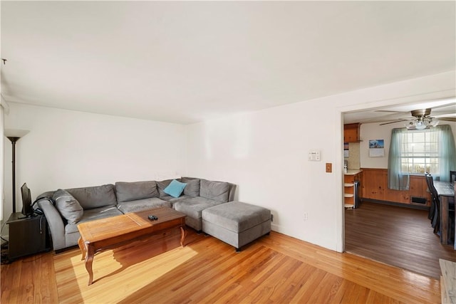 living area featuring a wainscoted wall, light wood finished floors, and ceiling fan