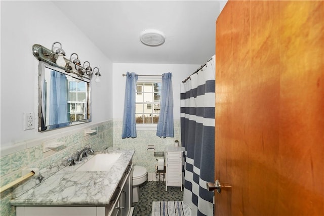 full bath featuring vanity, tile walls, toilet, and wainscoting