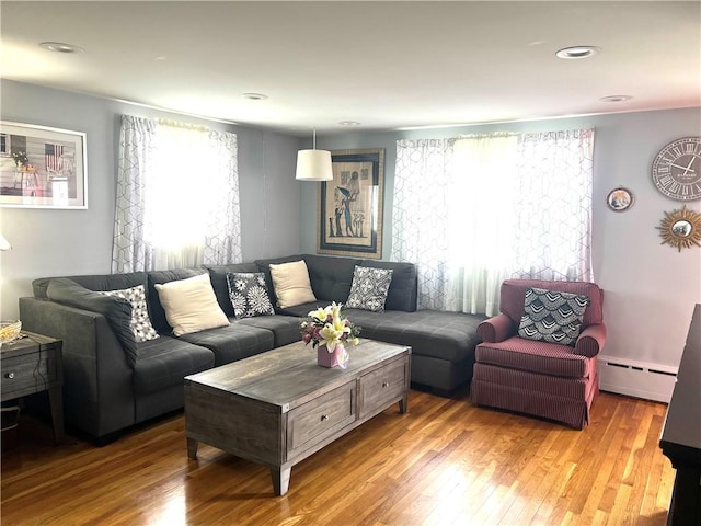 living area with wood finished floors, baseboard heating, and a healthy amount of sunlight