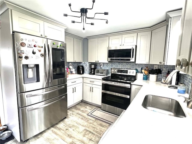 kitchen featuring appliances with stainless steel finishes, a sink, light countertops, gray cabinets, and backsplash