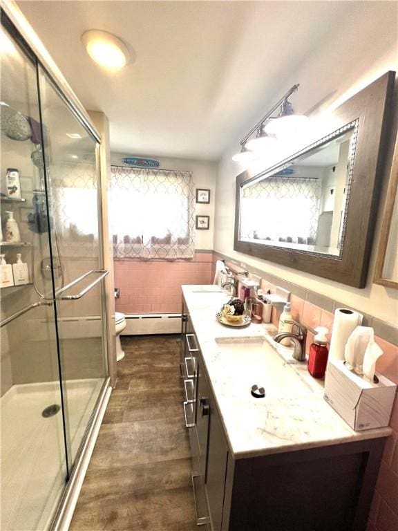 full bath featuring toilet, tile walls, a baseboard heating unit, a sink, and a stall shower
