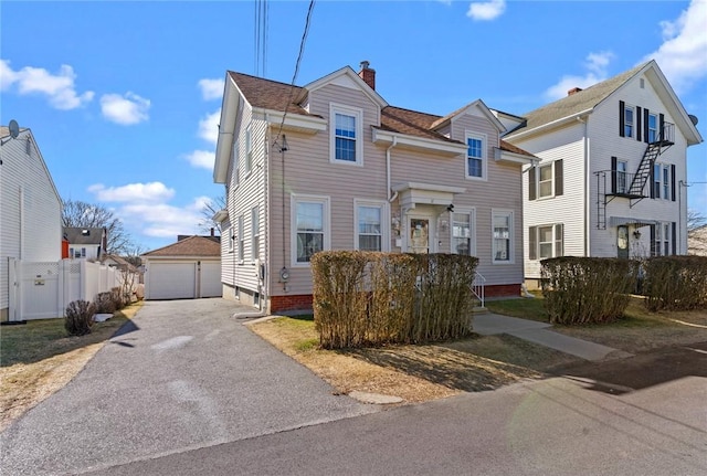 view of front facade featuring a detached garage, an outdoor structure, a chimney, and fence