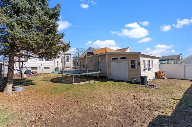 back of property with an outdoor structure, a trampoline, fence, and a yard