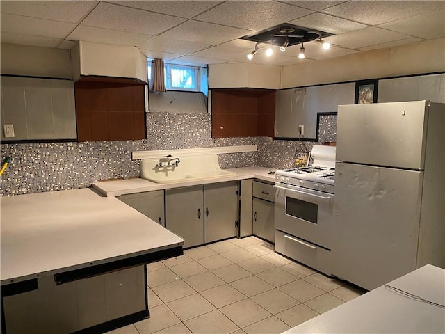 kitchen with white appliances, a drop ceiling, a sink, light countertops, and backsplash