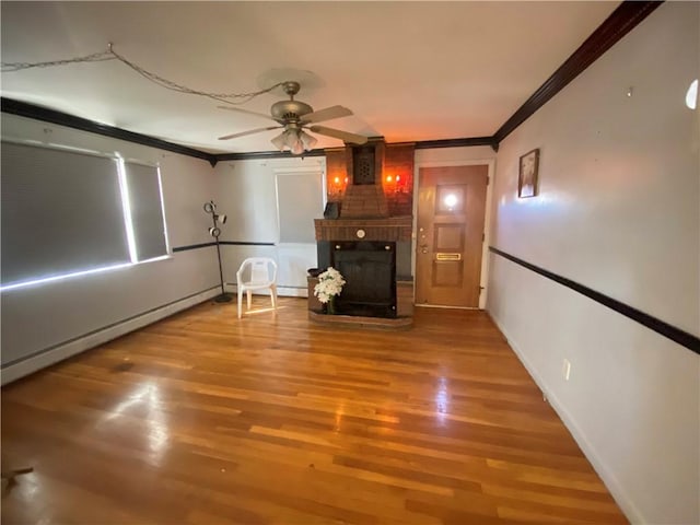 unfurnished living room with a ceiling fan, crown molding, wood finished floors, and a large fireplace