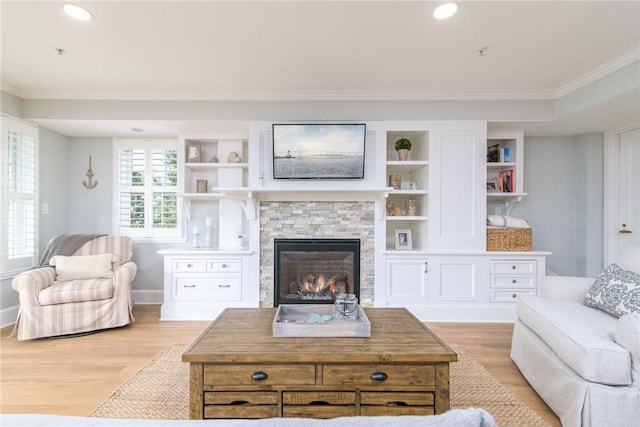 living room featuring a stone fireplace, built in features, light wood-style floors, and ornamental molding