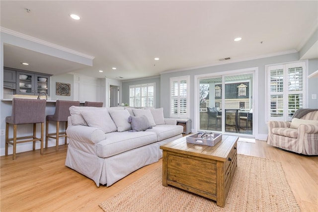 living area with visible vents, a healthy amount of sunlight, light wood-style flooring, and ornamental molding