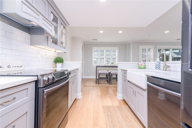 kitchen featuring decorative backsplash, light countertops, light wood-style flooring, and appliances with stainless steel finishes