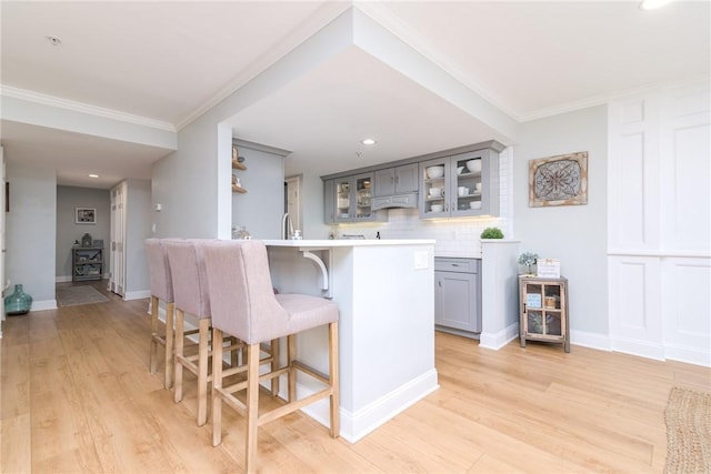 kitchen featuring light wood finished floors, gray cabinets, decorative backsplash, light countertops, and a kitchen breakfast bar