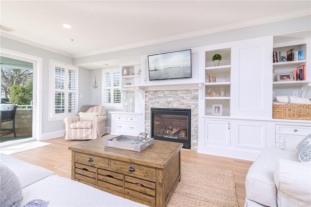 living room with a stone fireplace, built in shelves, light wood-style floors, and ornamental molding