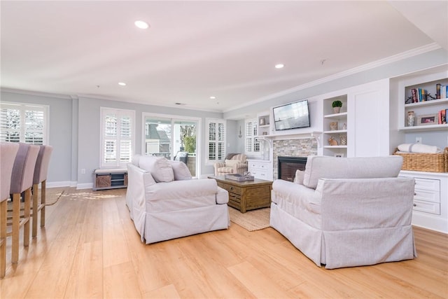 living area with a stone fireplace, a healthy amount of sunlight, light wood-type flooring, and ornamental molding