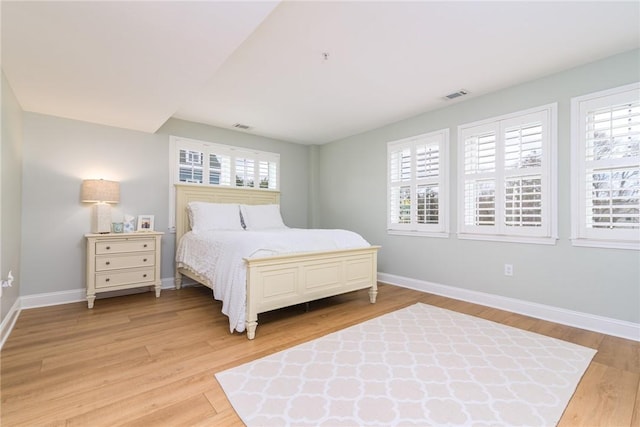 bedroom with light wood finished floors, visible vents, multiple windows, and baseboards