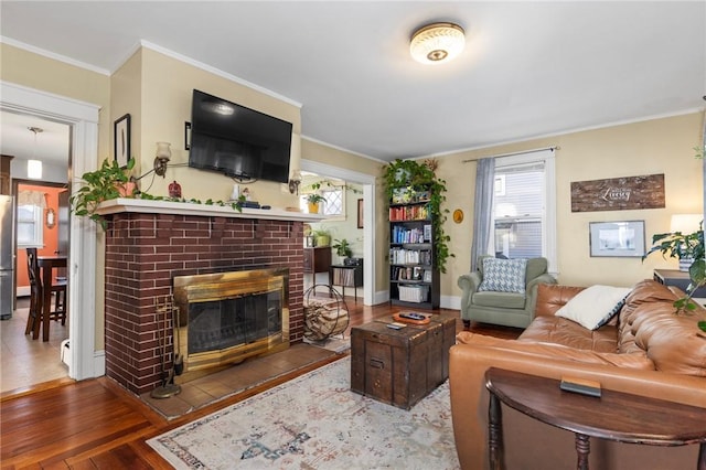 living room featuring a brick fireplace, crown molding, baseboards, and hardwood / wood-style floors