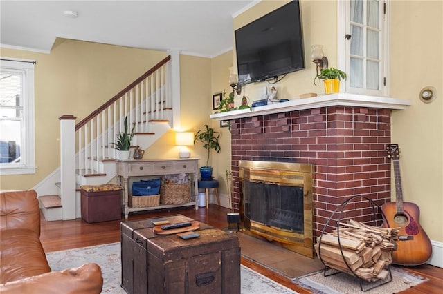 living area with stairs, wood finished floors, a fireplace, and crown molding