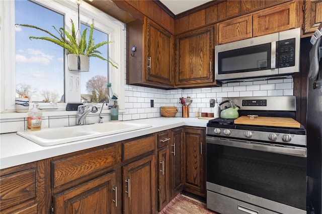 kitchen featuring tasteful backsplash, appliances with stainless steel finishes, light countertops, and a sink