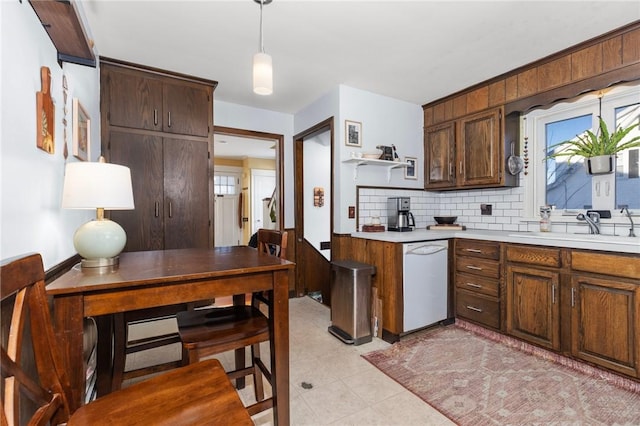 kitchen featuring a sink, tasteful backsplash, white dishwasher, light countertops, and hanging light fixtures