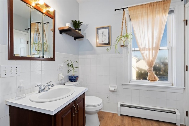 bathroom featuring toilet, wood finished floors, tile walls, baseboard heating, and vanity