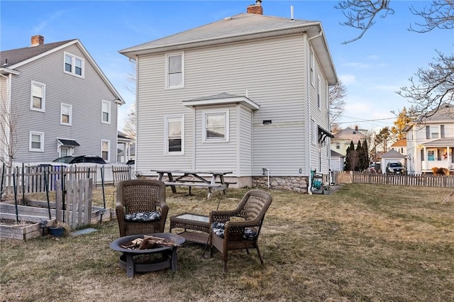 rear view of property with fence, a garden, a chimney, a fire pit, and a lawn