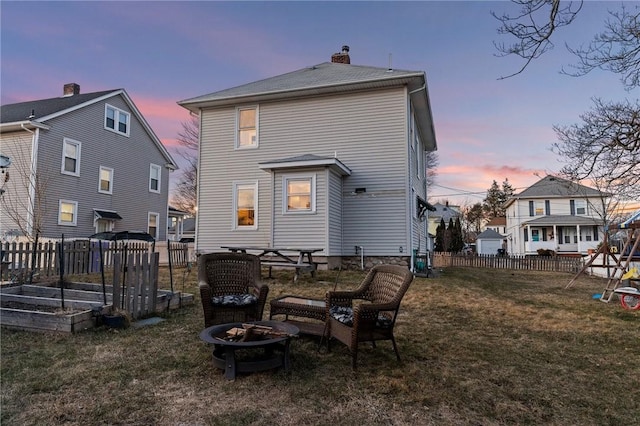 rear view of property with a lawn, an outdoor fire pit, fence, a garden, and a chimney