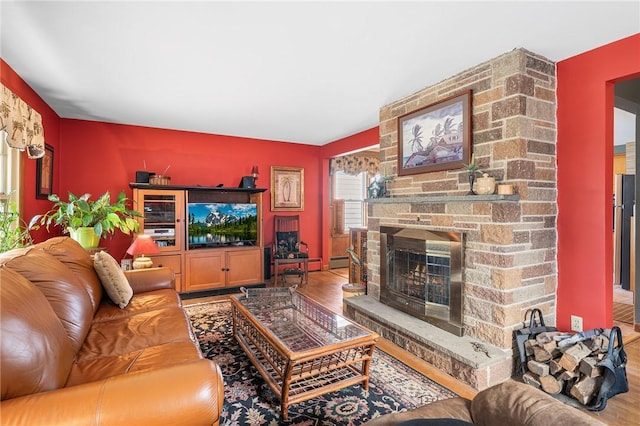 living area with a stone fireplace, a baseboard radiator, and wood finished floors