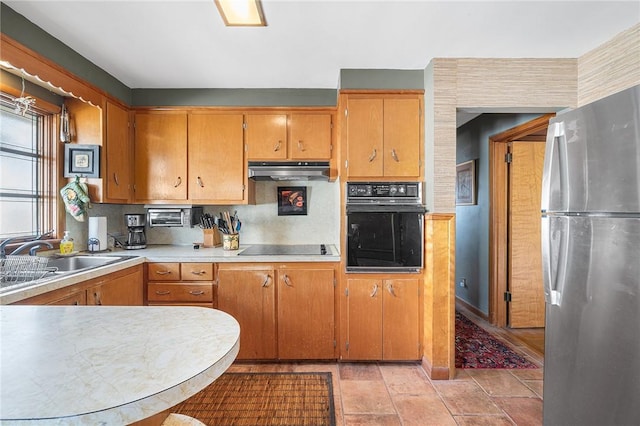 kitchen with a sink, black appliances, light countertops, under cabinet range hood, and brown cabinets