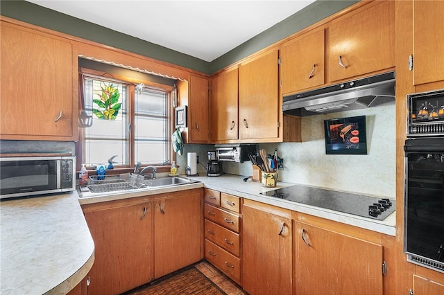 kitchen featuring a sink, decorative backsplash, black appliances, light countertops, and under cabinet range hood