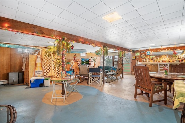 dining area featuring a baseboard heating unit, wood walls, and concrete floors