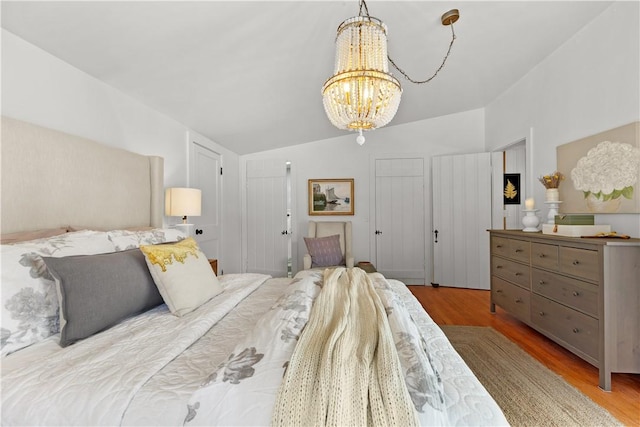 bedroom with lofted ceiling, a notable chandelier, and wood finished floors