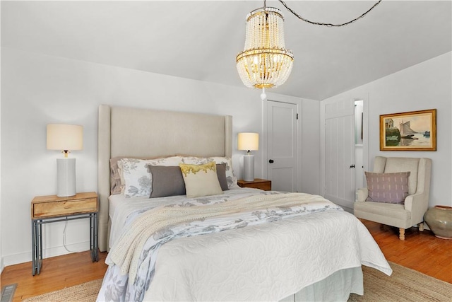 bedroom featuring a notable chandelier, visible vents, baseboards, and wood finished floors