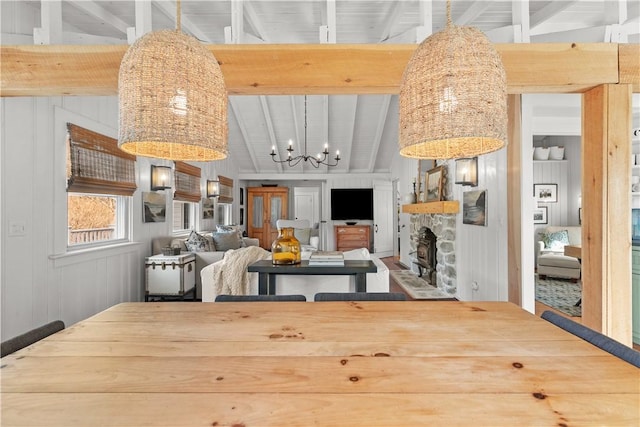 dining area featuring a stone fireplace, a chandelier, and vaulted ceiling with beams