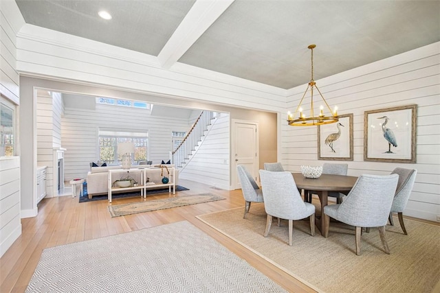 dining space featuring light wood finished floors, stairway, an inviting chandelier, and wooden walls