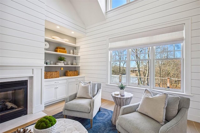 living area with a fireplace with flush hearth, wooden walls, vaulted ceiling, and light wood finished floors