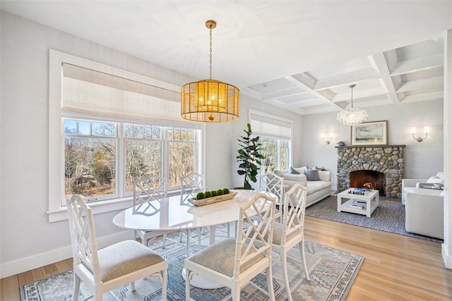 dining room featuring baseboards, coffered ceiling, beam ceiling, a stone fireplace, and light wood-type flooring