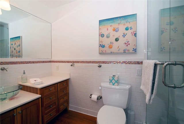 bathroom featuring toilet, a stall shower, wood finished floors, wainscoting, and vanity