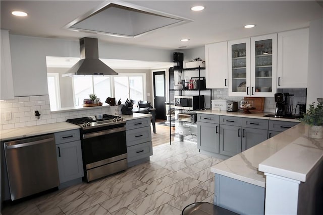 kitchen featuring light stone counters, stainless steel appliances, gray cabinetry, and island range hood