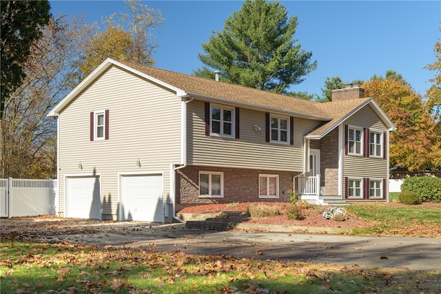 split foyer home featuring an attached garage, fence, and a chimney