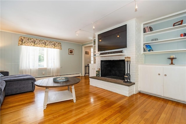 living area featuring light wood finished floors, baseboard heating, a brick fireplace, and crown molding