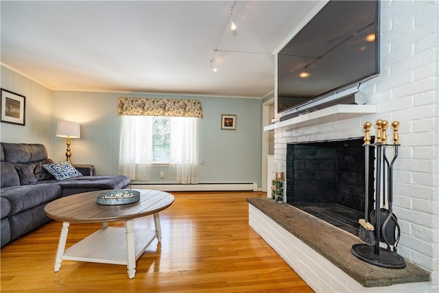 living room featuring light wood-type flooring, a baseboard heating unit, a fireplace, and ornamental molding