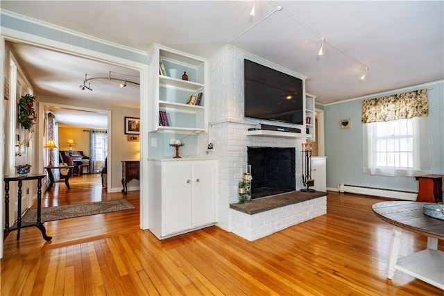 living room with light wood-type flooring, ornamental molding, a baseboard heating unit, rail lighting, and a brick fireplace