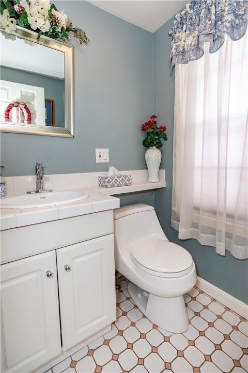 half bathroom with vanity, tile patterned floors, toilet, and baseboards